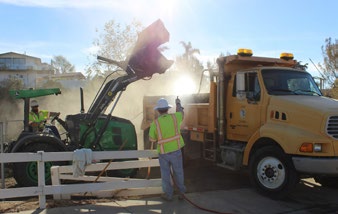 Crane is dumping stuff into the back of a truck.